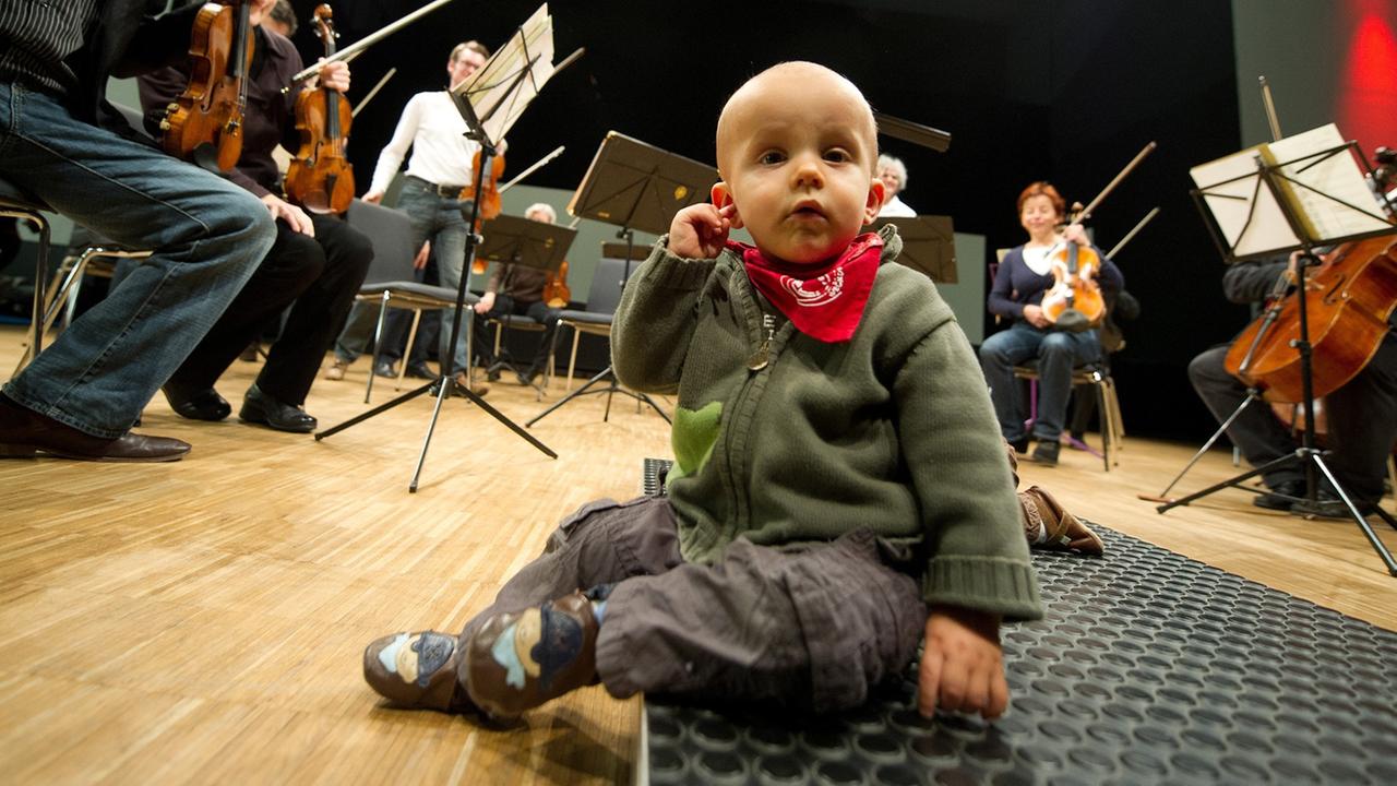 Der kleine Niklas fasst sich am 21.11.2012 in Heilbronn (Baden-Württemberg) vor Beginn des Babykonzerts des Württembergischen Kammerorchesters Heilbronn an sein Ohr. Eltern mit ihren Babys besuchten das ausverkaufte Konzert des Orchesters, das klassische Musik spielte. Der kleine Niklas fasst sich am 21.11.2012 in Heilbronn (Baden-Württemberg) vor Beginn des Babykonzerts des Württembergischen Kammerorchesters Heilbronn an sein Ohr. Eltern mit ihren Babys besuchten das ausverkaufte Konzert des Orchesters, das klassische Musik spielte.