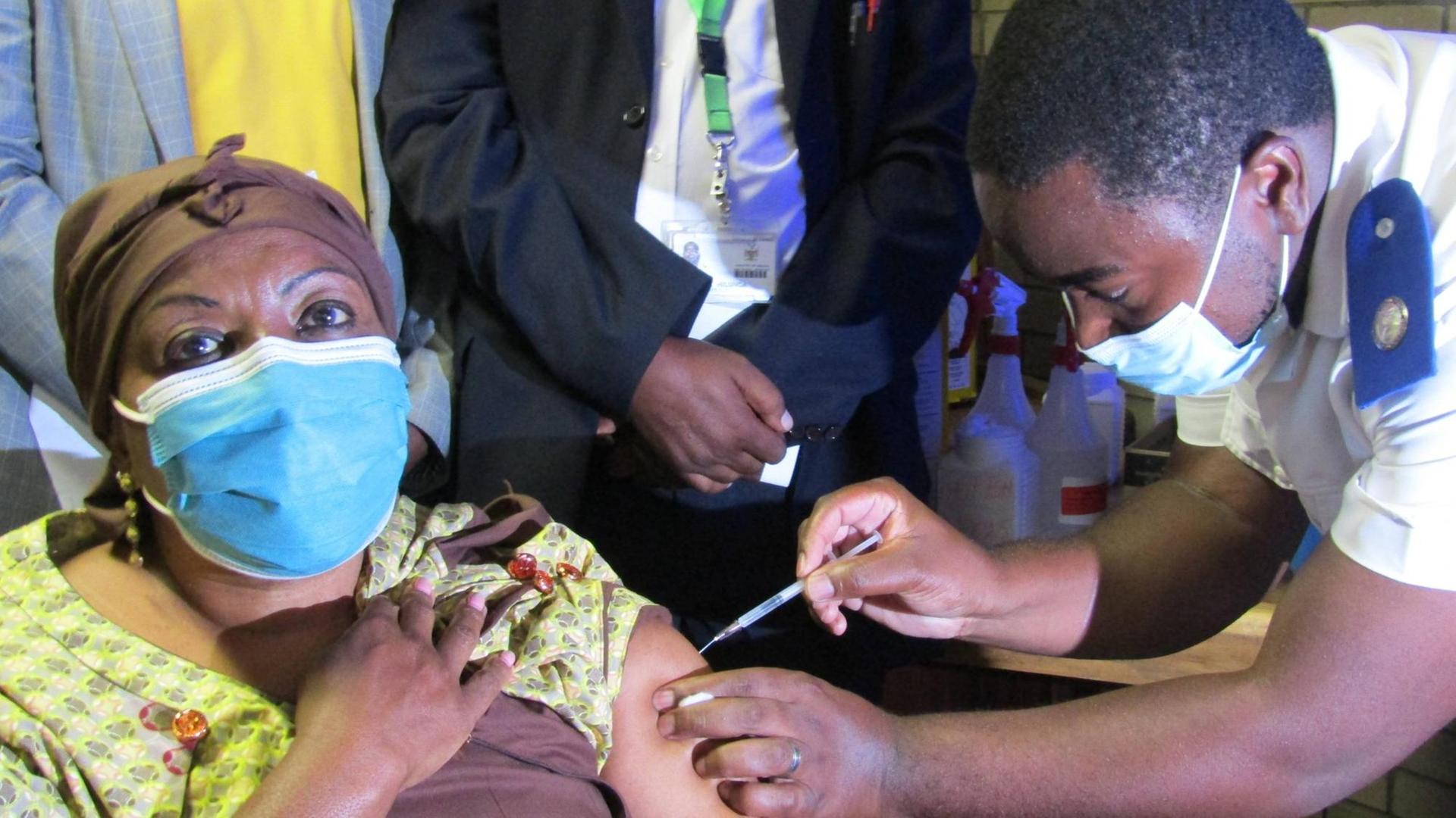 Die Gesundheitsminsterin von Namibia sitzt in einem gelben Kleid auf einem Stuhl und wird von einem Arzt geimpft Die Gesundheitsminsterin von Namibia sitzt in einem gelben Kleid auf einem Stuhl und wird von einem Arzt geimpft