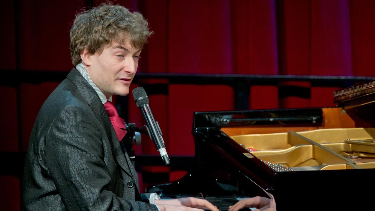 Der Kabarettist Sebastian Krämer sitzt singend am Klavier. Der Kabarettist Sebastian Krämer sitzt singend am Klavier.