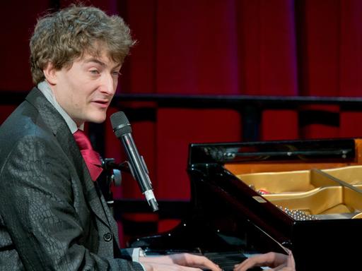 Der Kabarettist Sebastian Krämer sitzt singend am Klavier.