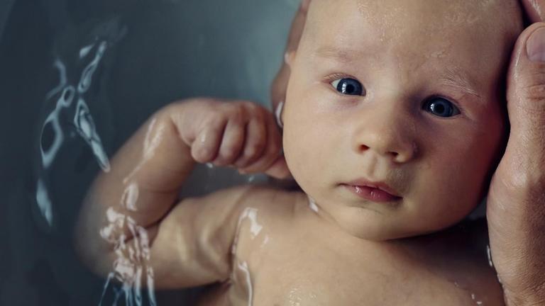 Ein Baby wird gebadet und schaut geradewegs in die Kamera. Um den Kopf ist eine schützende Hand gelegt. (Symbolfoto) Ein Baby wird gebadet und schaut geradewegs in die Kamera. Um den Kopf ist eine schützende Hand gelegt. (Symbolfoto)