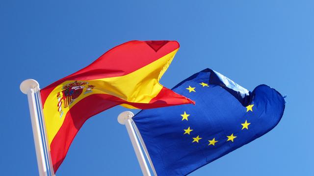 Spaniens Flagge und Europafahne wehen vor blauem Himmel im Wind.