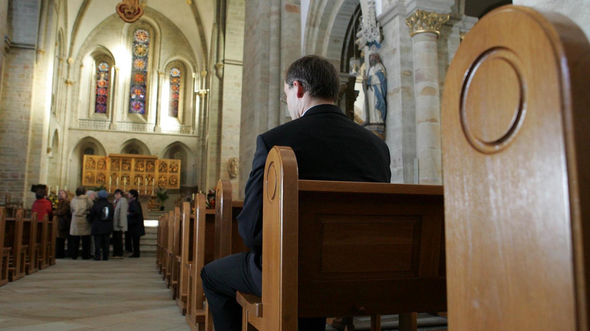 Ein Pfarrer sitzt in einer Kirchenbank und betet.