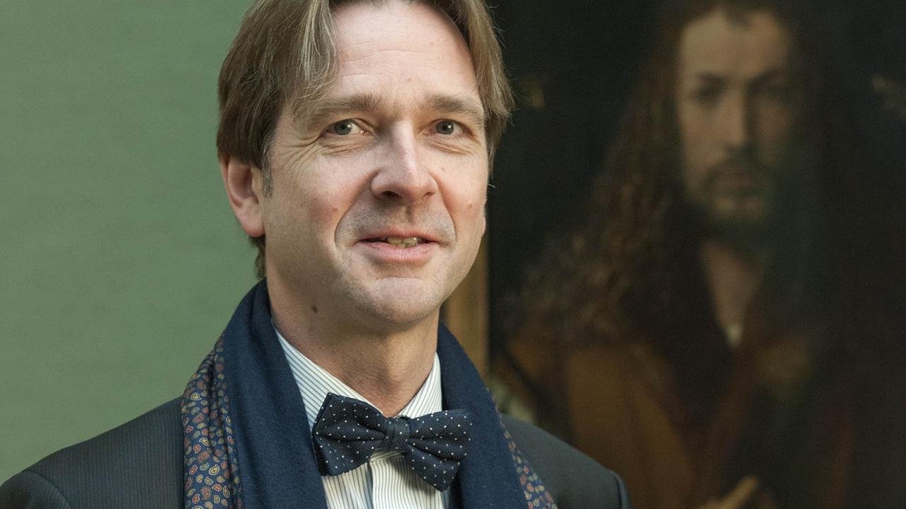 Bernhard Maaz, mit hellbraunen Haaren, in Anzug und Fliege, steht lächelnd vor einem Jesus-Portrait Albrecht Dürers. Bernhard Maaz, mit hellbraunen Haaren, in Anzug und Fliege, steht lächelnd vor einem Jesus-Portrait Albrecht Dürers.