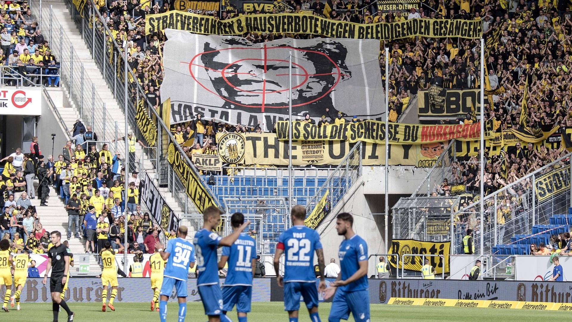 Man sieht das Spielfeld im Stadion der TSG Hoffenheim. Im Hintergrund haben BVB-Fans ein großes Banner mit dem Konterfei von Hoffenheim-Mäzen Dietmar Hopp mit einem Fadenkreuz entrollt. Man sieht das Spielfeld im Stadion der TSG Hoffenheim. Im Hintergrund haben BVB-Fans ein großes Banner mit dem Konterfei von Hoffenheim-Mäzen Dietmar Hopp mit einem Fadenkreuz entrollt.