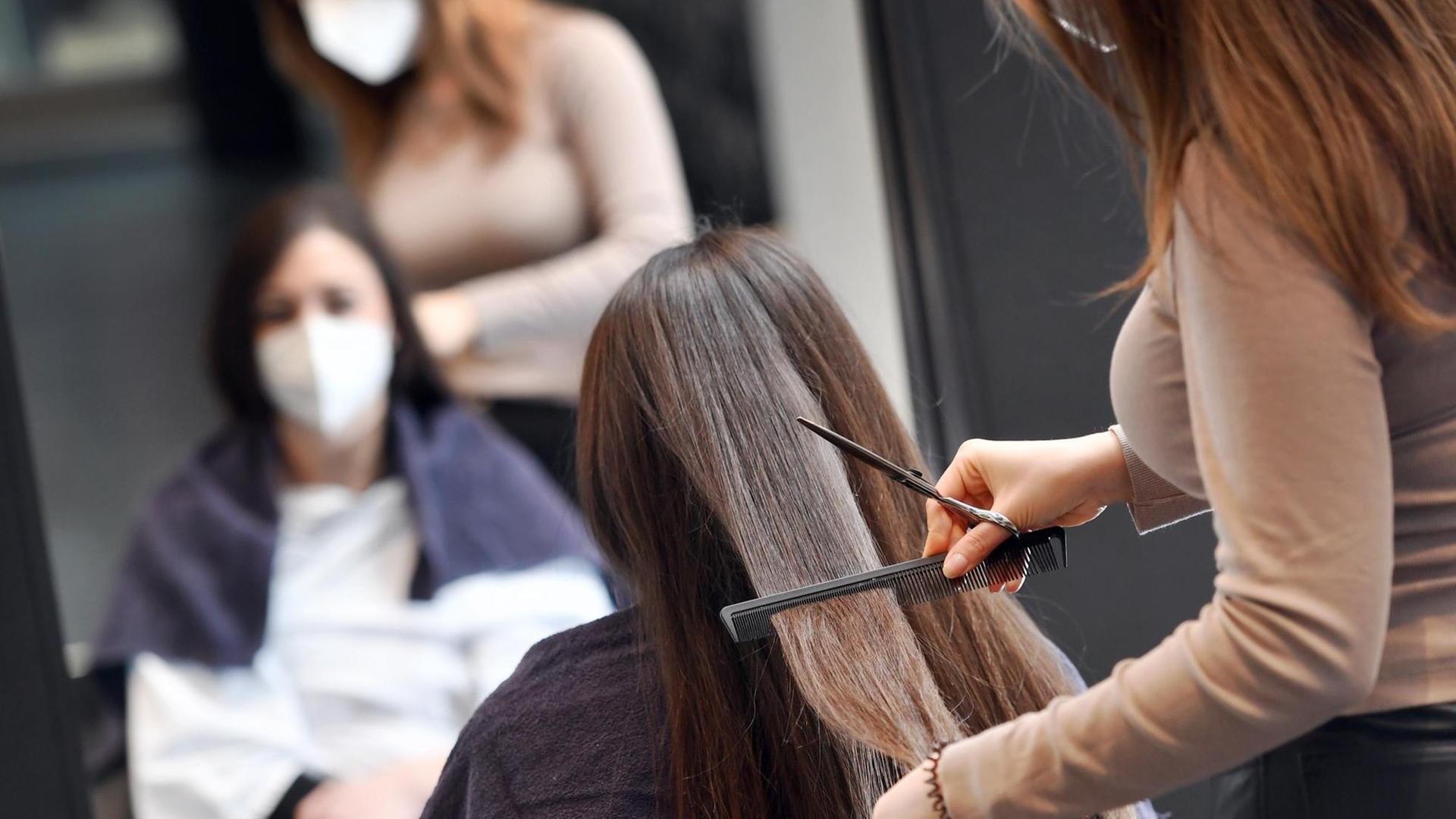 Eine Friseurin kämmt einer Frau die Haare, beide tragen Masken Eine Friseurin kämmt einer Frau die Haare, beide tragen Masken