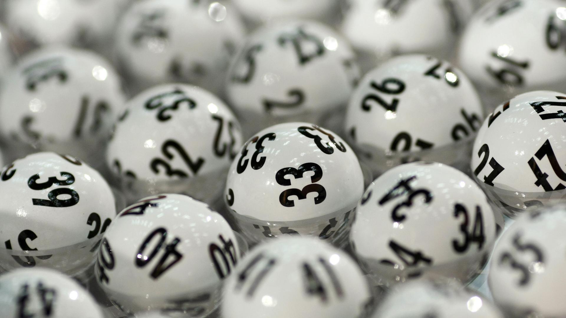 Das Bild zeigt ein gutes Dutzend weiße Lotto-Kugeln, die mit schwarzen Zahlen bedruckt sind. 