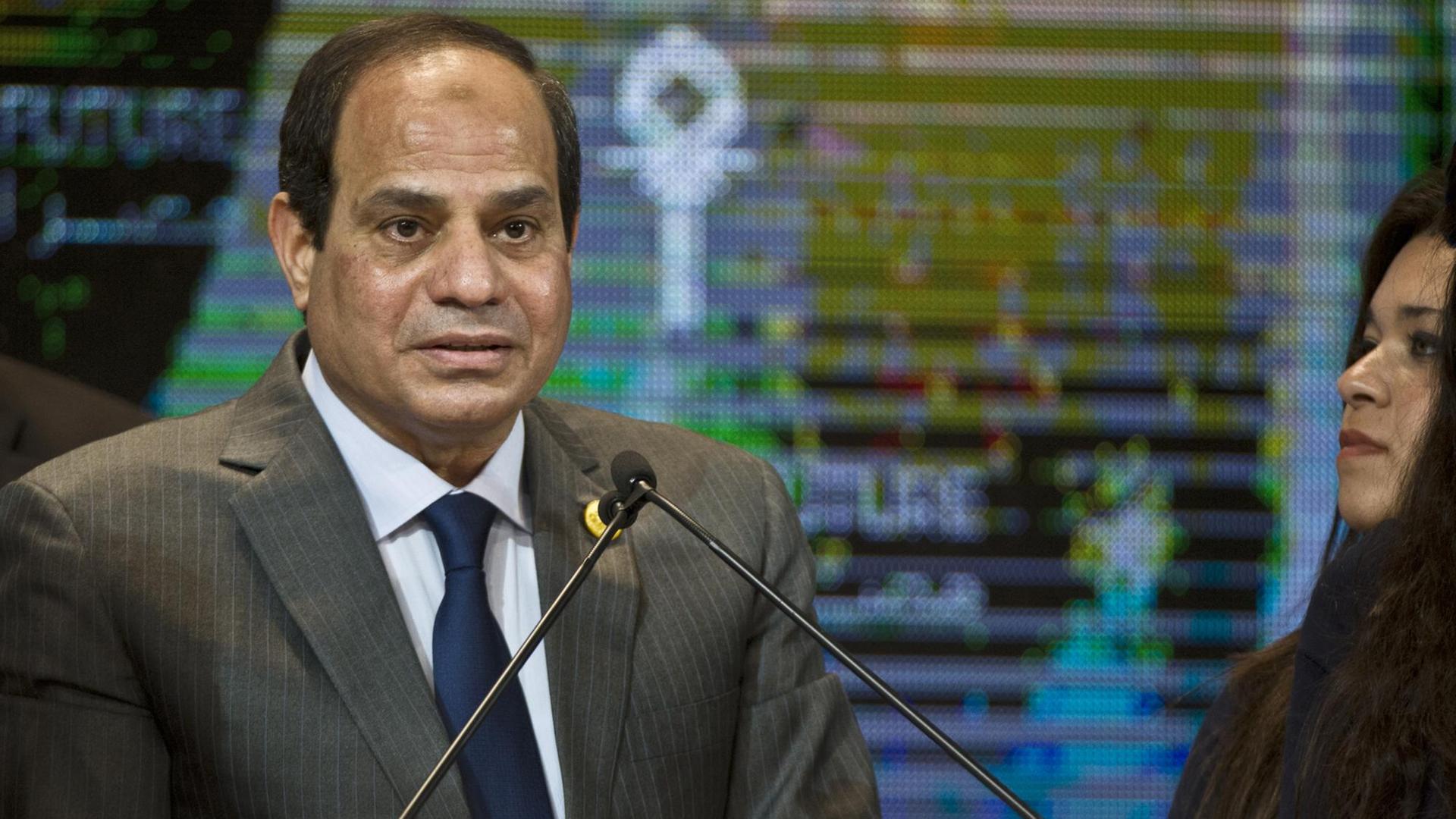 Der ägyptische Präsident Abdelfatah al-Sisi spricht an einem Rednerpult. Hinter ihm ist ein bunte TV-Leinwand zu sehen. Am rechten Rand blickt ihn eine Frau mit langen schwarzen Haaren an. Der ägyptische Präsident Abdelfatah al-Sisi spricht an einem Rednerpult. Hinter ihm ist ein bunte TV-Leinwand zu sehen. Am rechten Rand blickt ihn eine Frau mit langen schwarzen Haaren an.