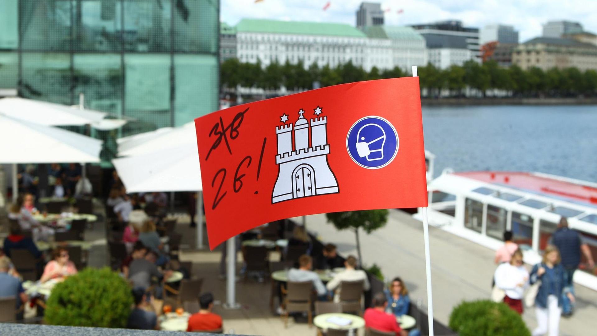 Eine Pappflagge mit dem Hamburg-Wappen sowie der Aufschrift 2G steckt in einer Mauer in der Hamburger Innenstadt vor einem Restaurant an der Alster. Eine Pappflagge mit dem Hamburg-Wappen sowie der Aufschrift 2G steckt in einer Mauer in der Hamburger Innenstadt vor einem Restaurant an der Alster.