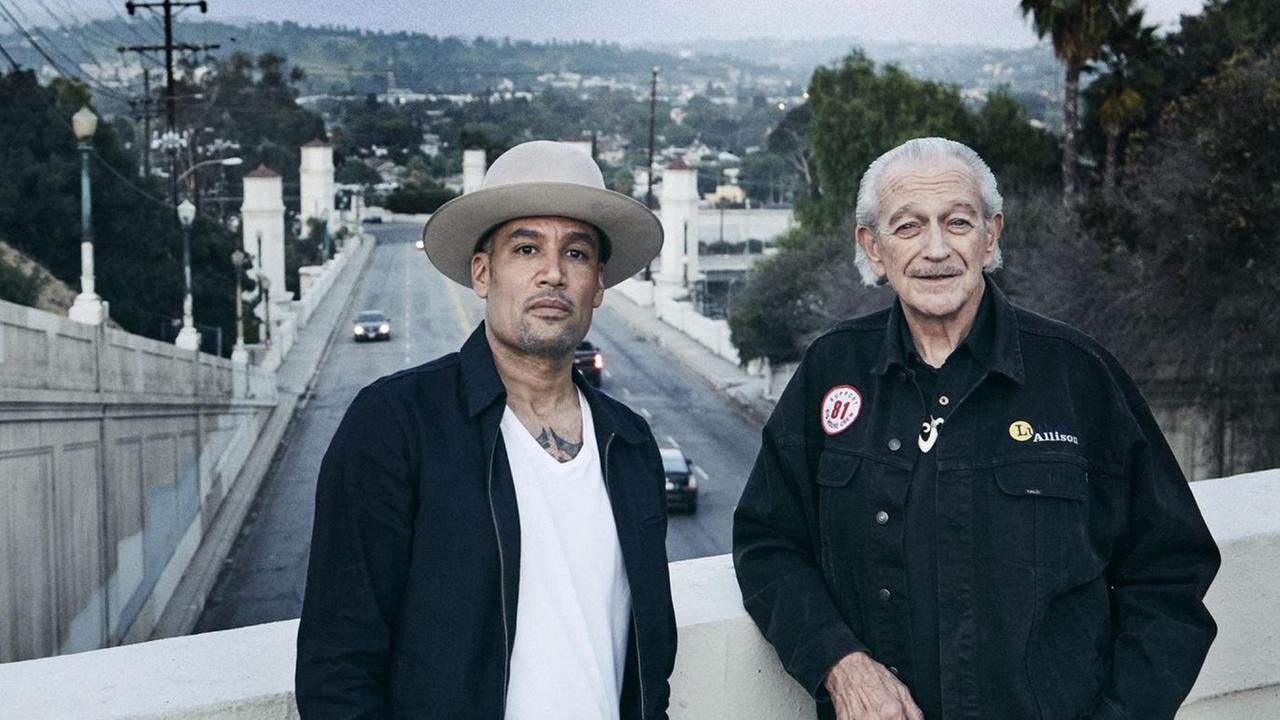 Ben Harper & Charlie Musselwhite stehen auf einer Brücke. Im Hintergrund ist eine Straße und ein Stadtrand vor Bergen zu erkennen. Ben Harper & Charlie Musselwhite stehen auf einer Brücke. Im Hintergrund ist eine Straße und ein Stadtrand vor Bergen zu erkennen.