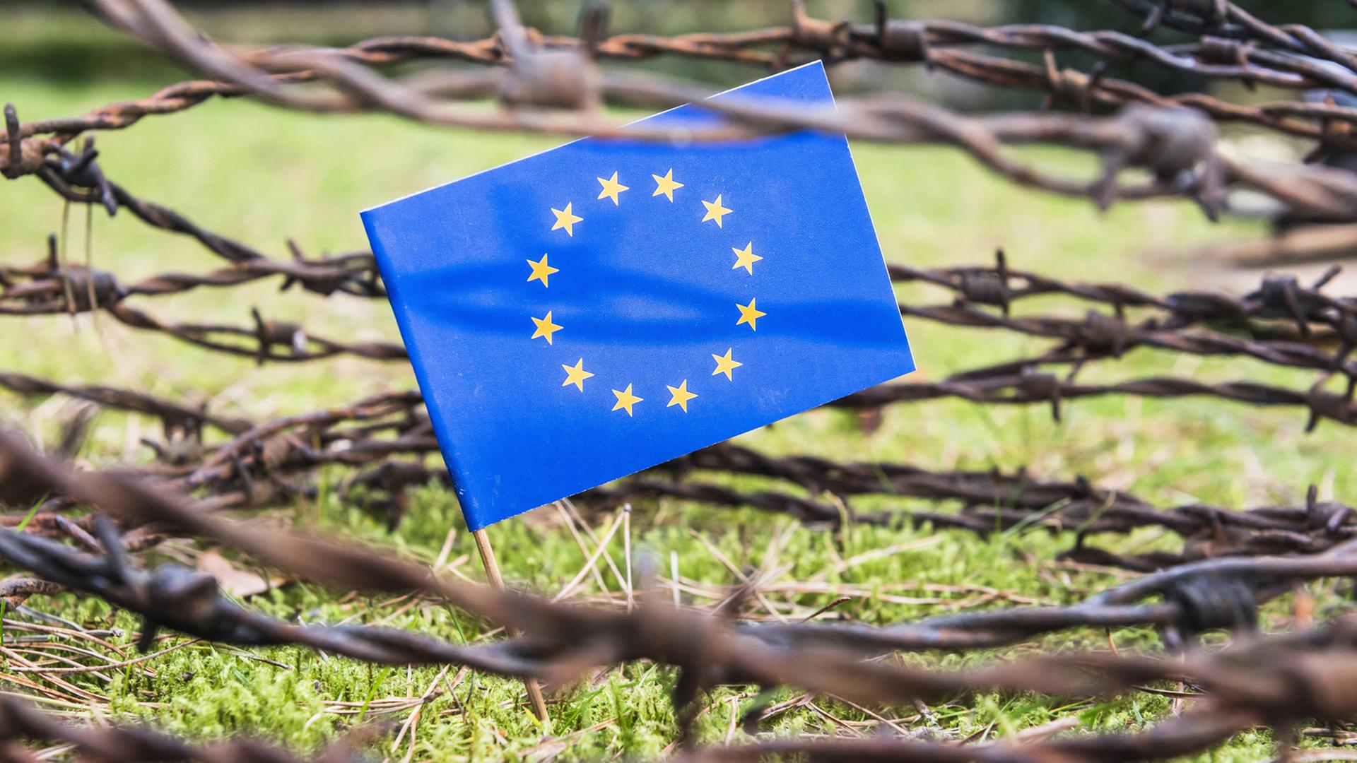 Flagge der EU hinter Stacheldrahtzaun