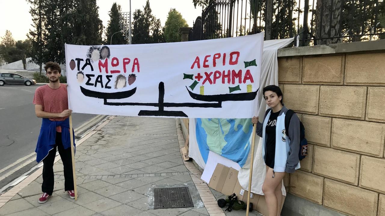 Die zwei jungen Aktivisten stehen mit einem bemalten Transparent an der Straße vor einer Mauer.