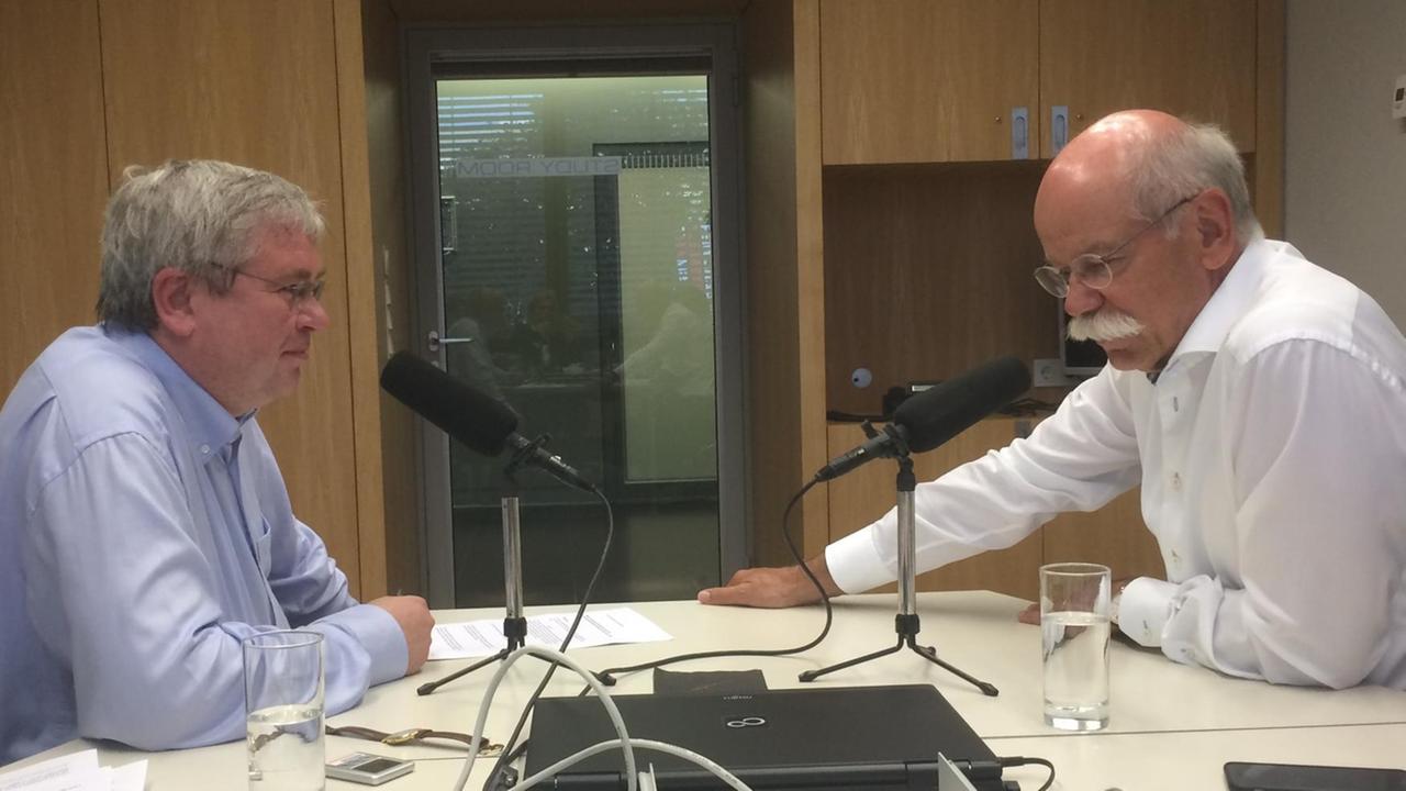 Klemens Kindermann und Dieter Zetsche sitzen sich an einem Tisch gegenüber, auf dem zwei Mikrofone stehen. Klemens Kindermann und Dieter Zetsche sitzen sich an einem Tisch gegenüber, auf dem zwei Mikrofone stehen.