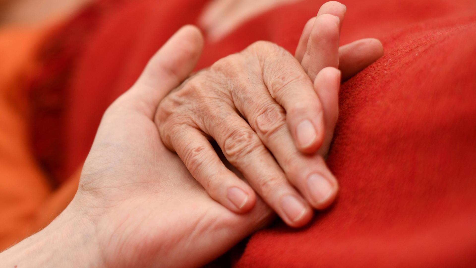 Die Hand eines alten Menschen wird von einer jüngeren Hand gehalten. 