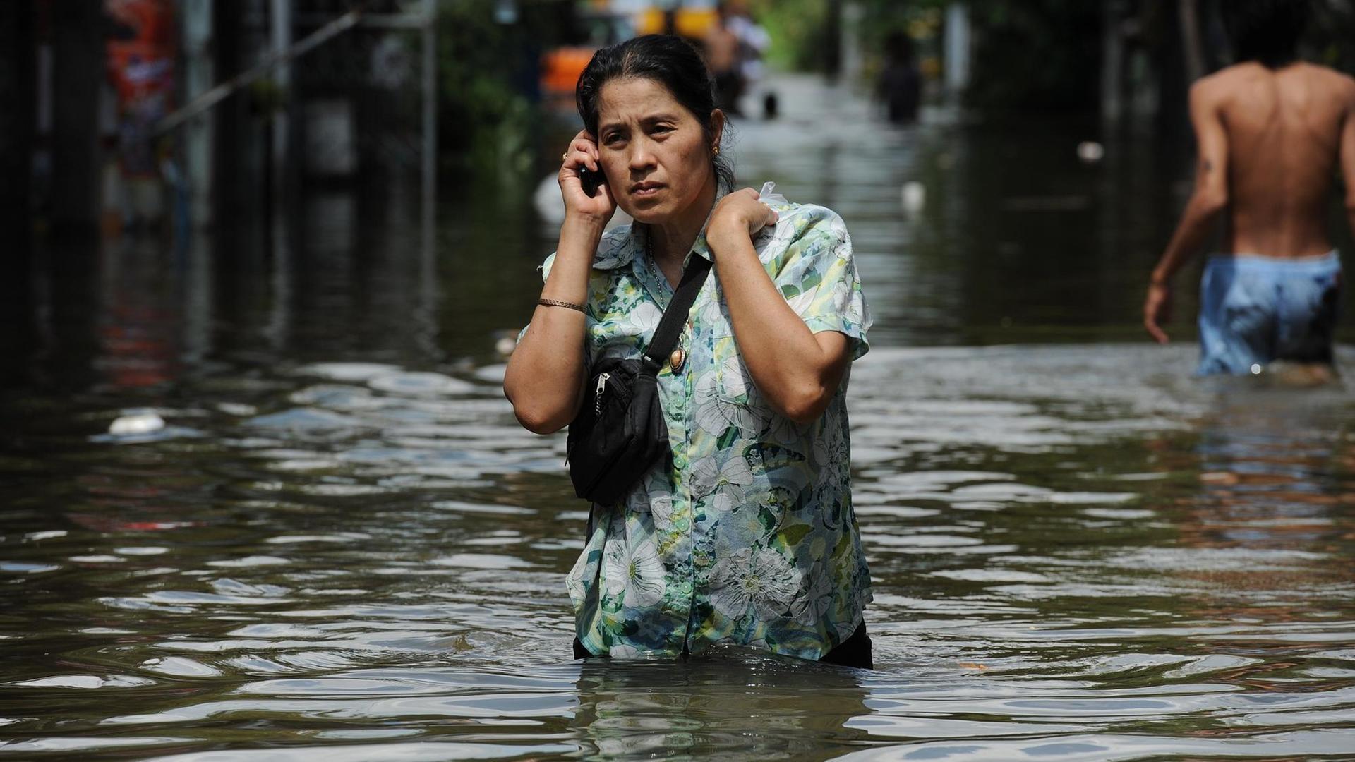 Eine Frau steht hüfthoch im Hochwasser und telefoniert per Handy Eine Frau steht hüfthoch im Hochwasser und telefoniert per Handy