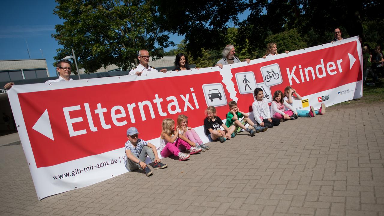 Schüler der Albert-Schweitzer-Grundschule in Hannover stellen mit Vertretern von Polizei und Schule mit einem Banner das Pilotprojekt "Eltern-Taxi" vor. Das sieht u.a. temporäre Straßensperrungen vor.