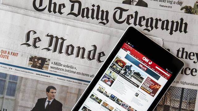Das Touchscreen eines digitalen Tablets zeigt die CNN International online Nachrichten, welches auf den beiden Zeitungen, der britische "The daily Telegraph" und der französischen "Le monde" liegt.