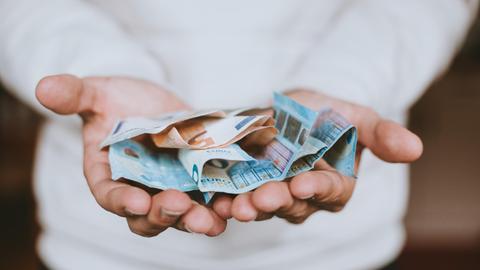 Zwei Hände reichen in Richtung des Betrachters mehrere Euro-Banknoten.