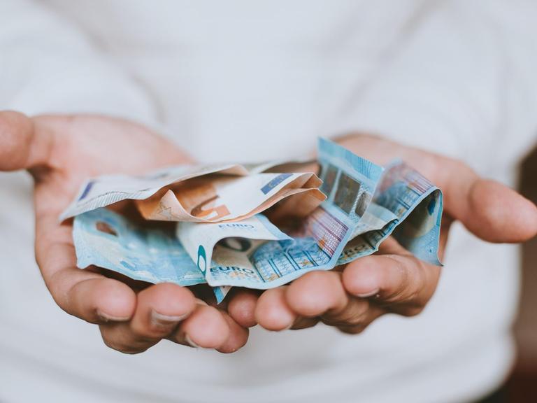 Zwei Hände reichen in Richtung des Betrachters mehrere Euro-Banknoten.