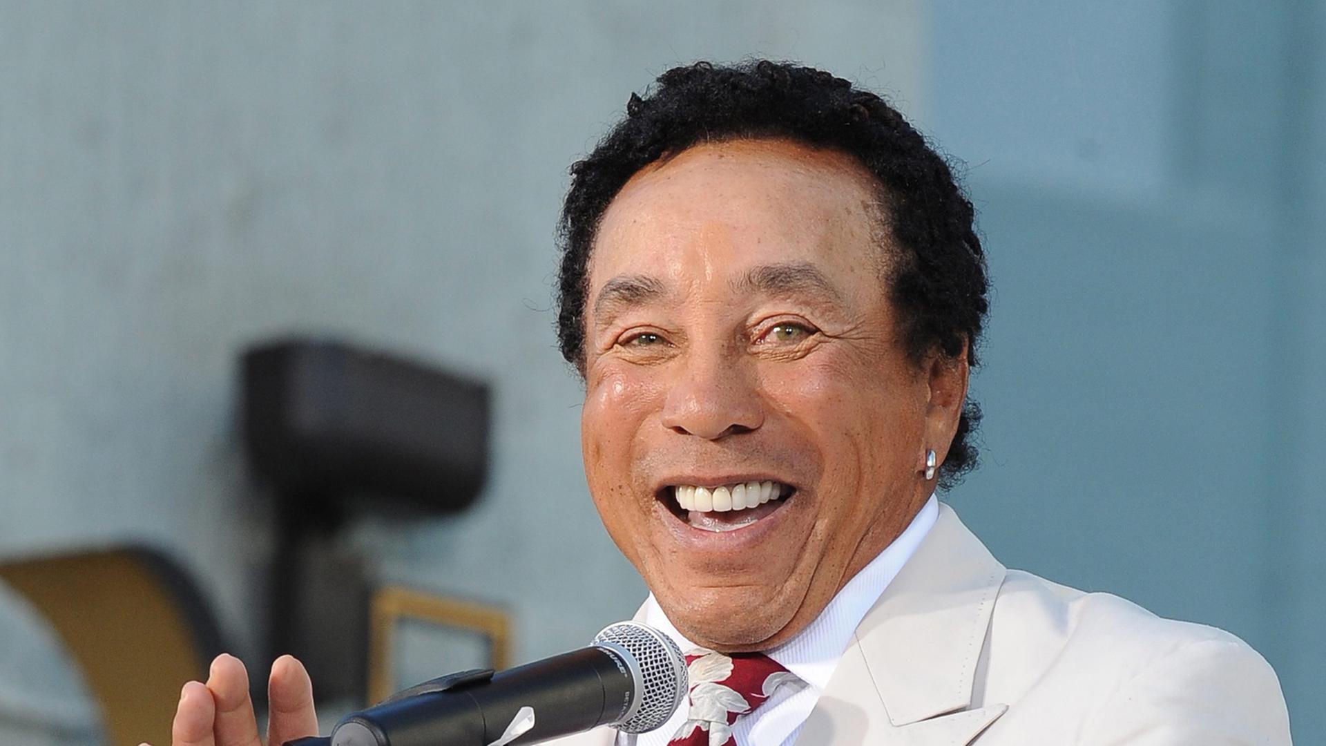 Der amerikanische Sänger und Songschreiber Smokey Robinson steht im weißen Anzug an einem Rednerpult. Der amerikanische Sänger und Songschreiber Smokey Robinson steht im weißen Anzug an einem Rednerpult.