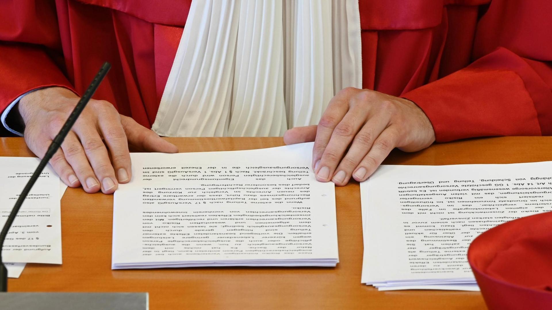 Die Hände eines Richter in roter Robe des Bundesverfassungsgerichts und das Urteil auf dem Tisch Die Hände eines Richter in roter Robe des Bundesverfassungsgerichts und das Urteil auf dem Tisch