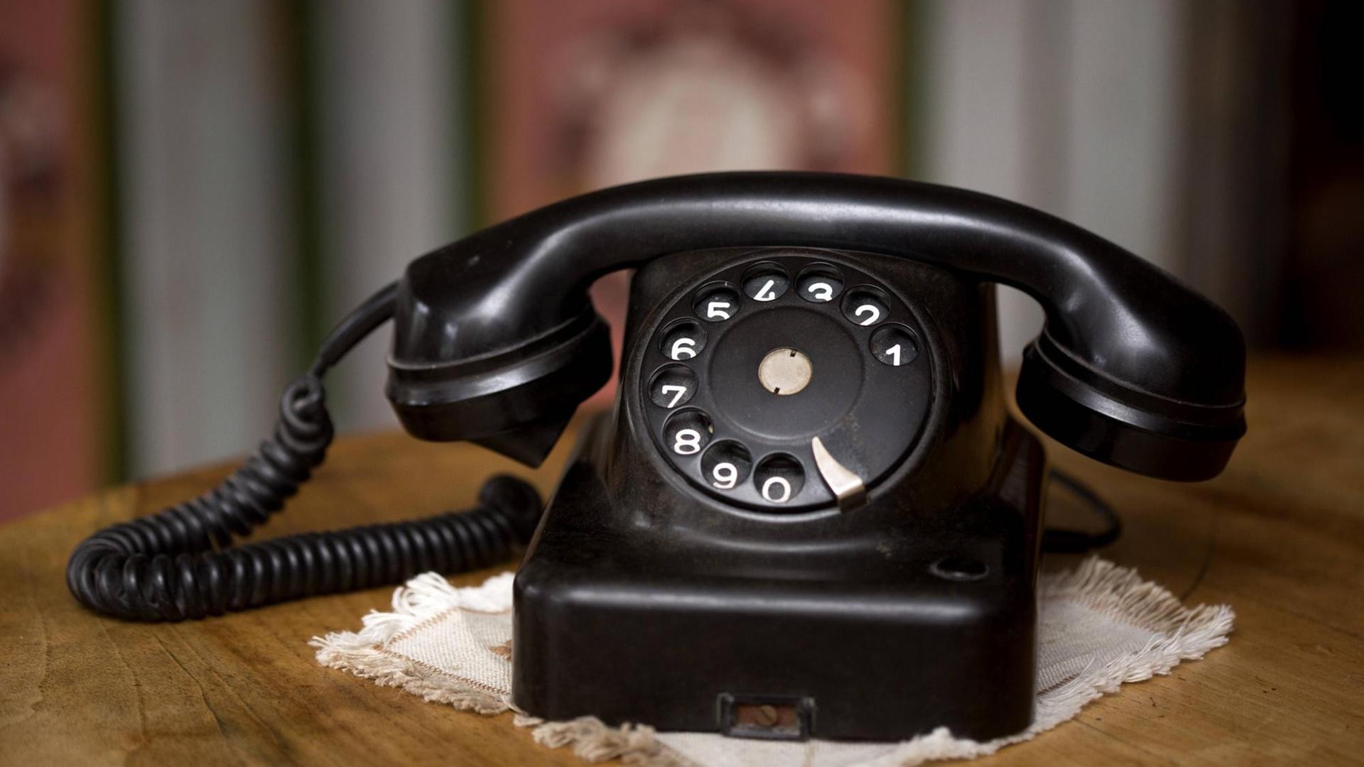 Ein alter Telefonapparat aus Bakelit steht auf einem Holzschränkchen