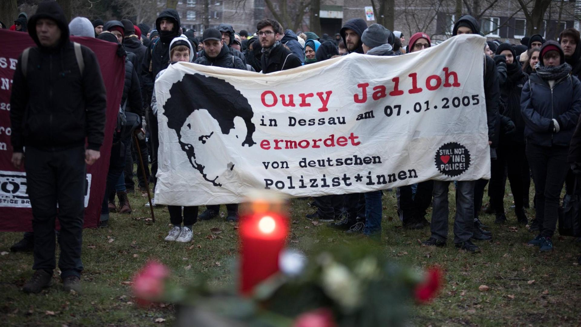 Demonstrierende halten ein Banner, auf dem steht: Oury Jalloh in Dessau am 07.01.2005 ermordet von deutschen Polizist*innen. Demonstrierende halten ein Banner, auf dem steht: Oury Jalloh in Dessau am 07.01.2005 ermordet von deutschen Polizist*innen.