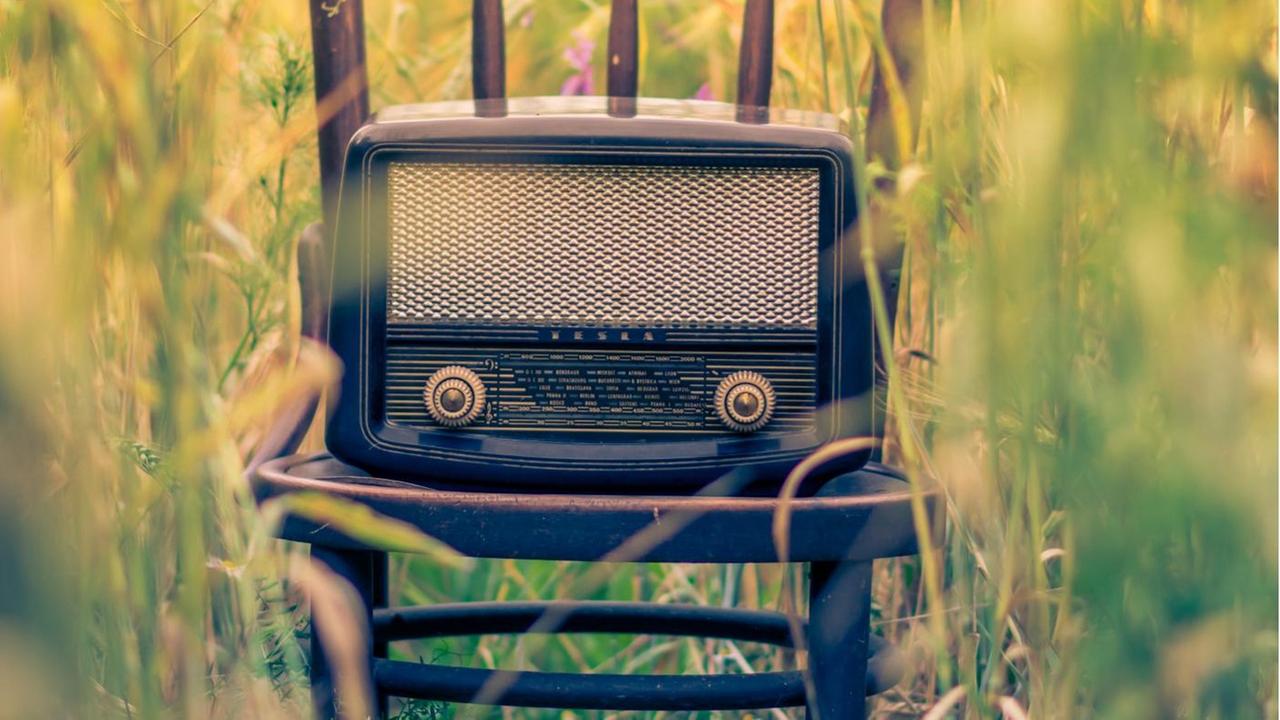 Ein altes Transistorradio steht auf einem Stuhl in der Mitte eines Feldes Ein altes Transistorradio steht auf einem Stuhl in der Mitte eines Feldes