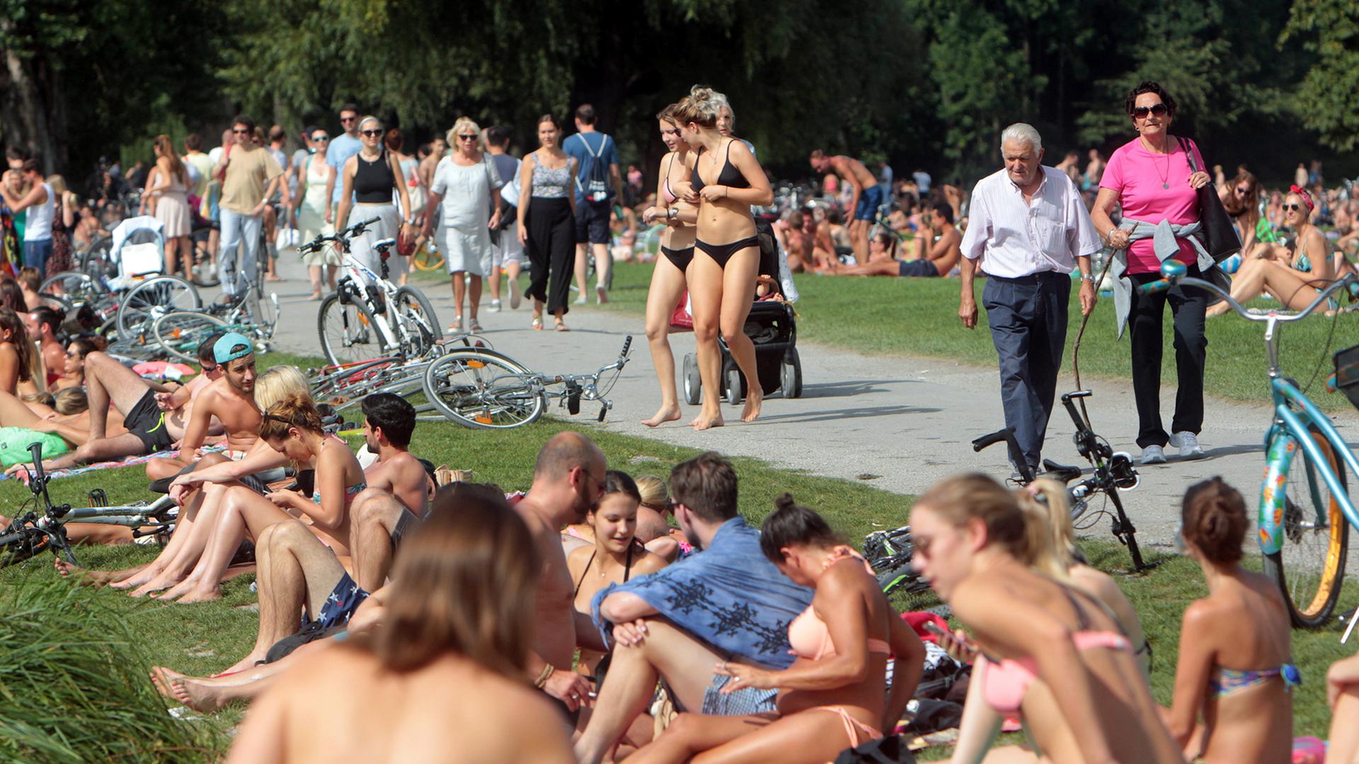 Großer Besucherandrang an Sonnenhungrigen und Spaziergängern sowie Touristen am Eisbach im Englischen Garten an einem heißen Sommertag in München.