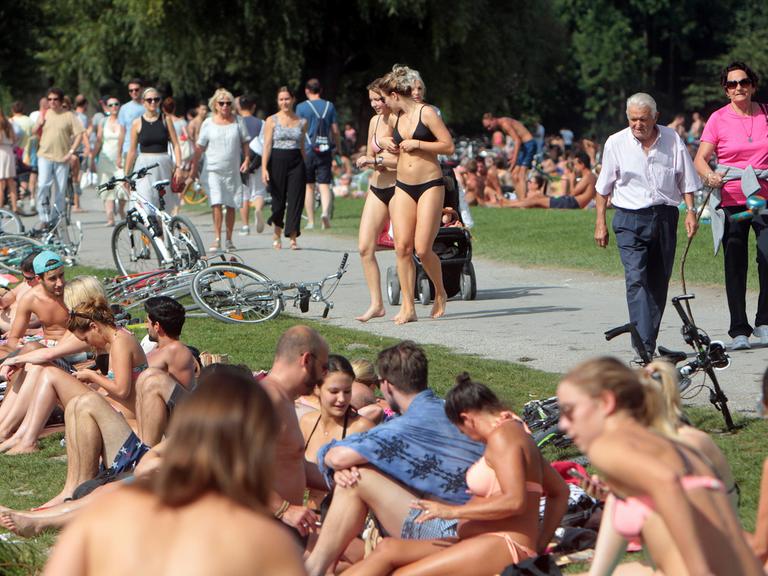 Großer Besucherandrang an Sonnenhungrigen und Spaziergängern sowie Touristen am Eisbach im Englischen Garten an einem heißen Sommertag in München.