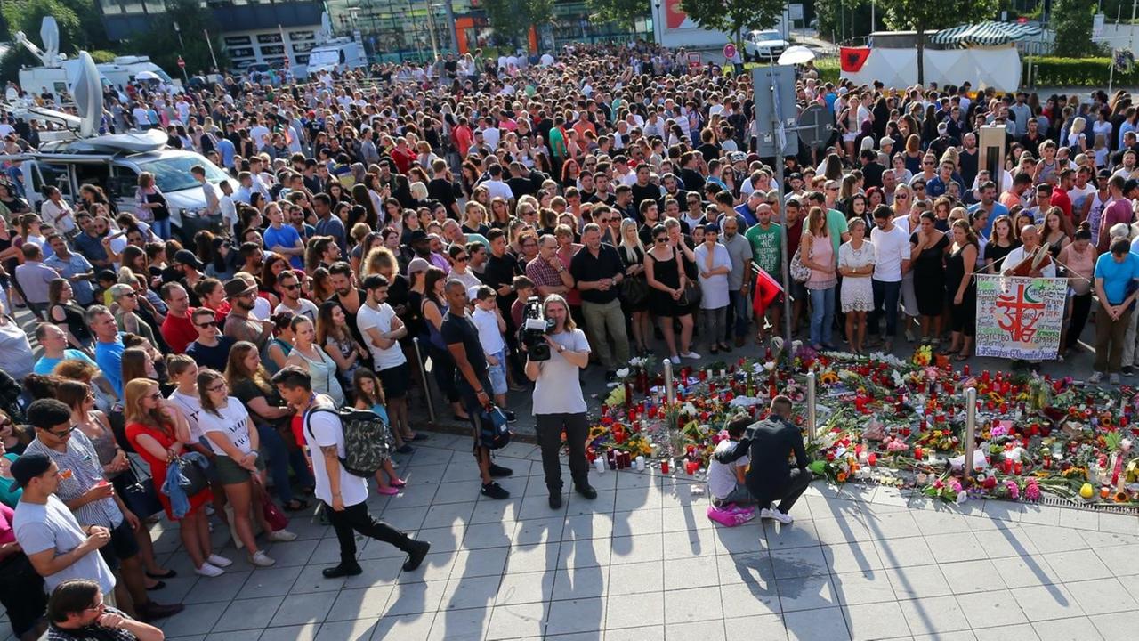 Sie sehen eine Menschenmenge von schräg oben herab fotografiert, davor liegen Blumen. Sie sehen eine Menschenmenge von schräg oben herab fotografiert, davor liegen Blumen.
