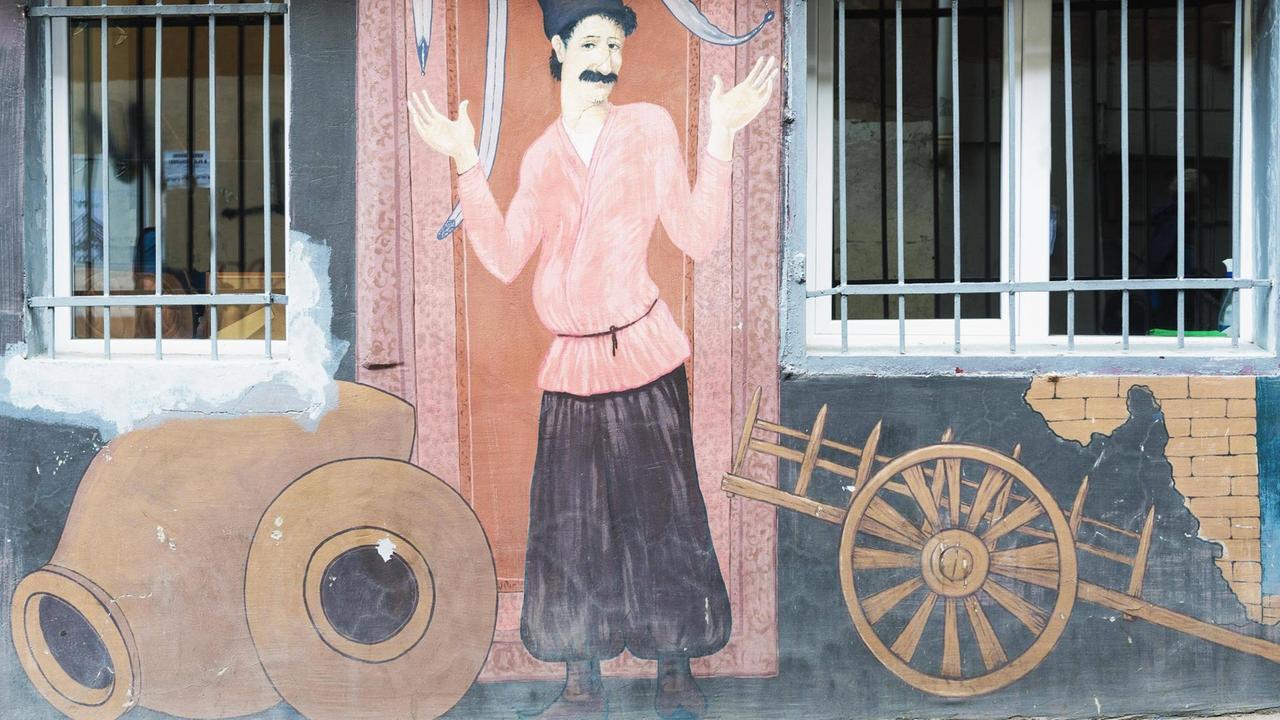 Das Wandgemälde zeigt einen Georgier in seiner Tracht, neben dem ein traditioneller Holzkarren mit zwei Rädern abgebildet ist.