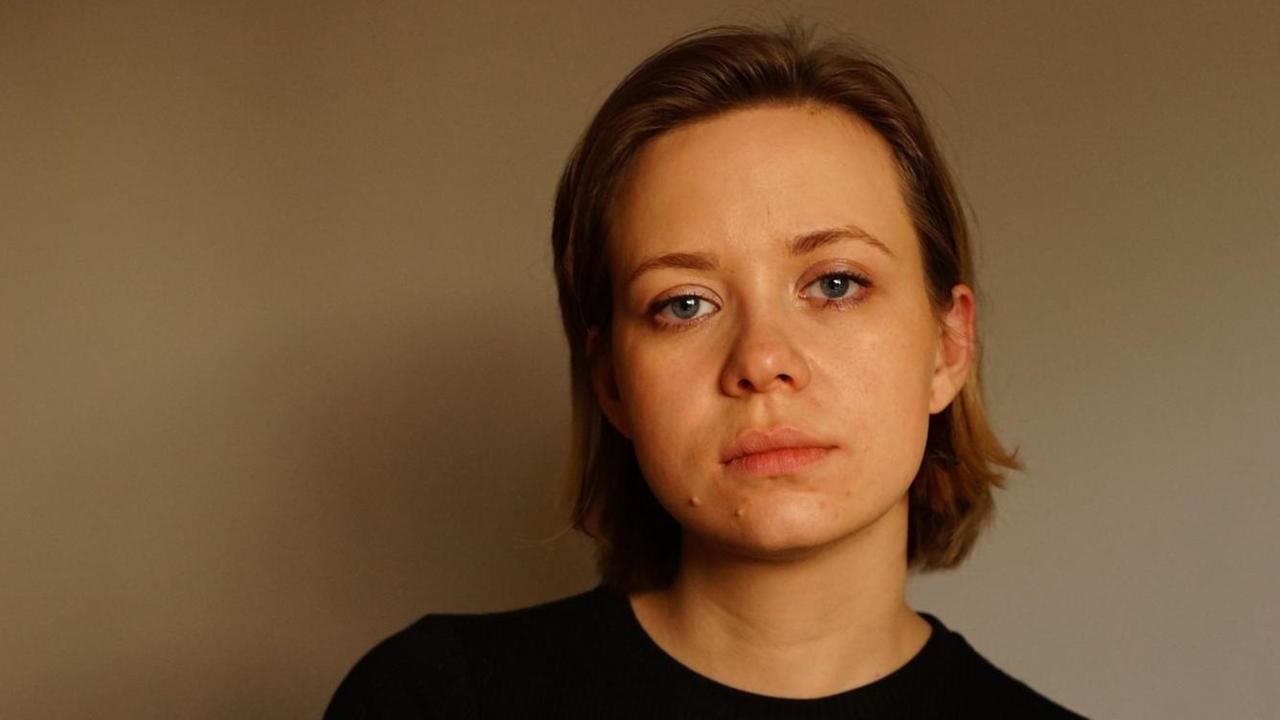 Eine junge Frau mit langen Haaren und in einem schwarzen T-Shirt steht vor einer Wand. Eine junge Frau mit langen Haaren und in einem schwarzen T-Shirt steht vor einer Wand.