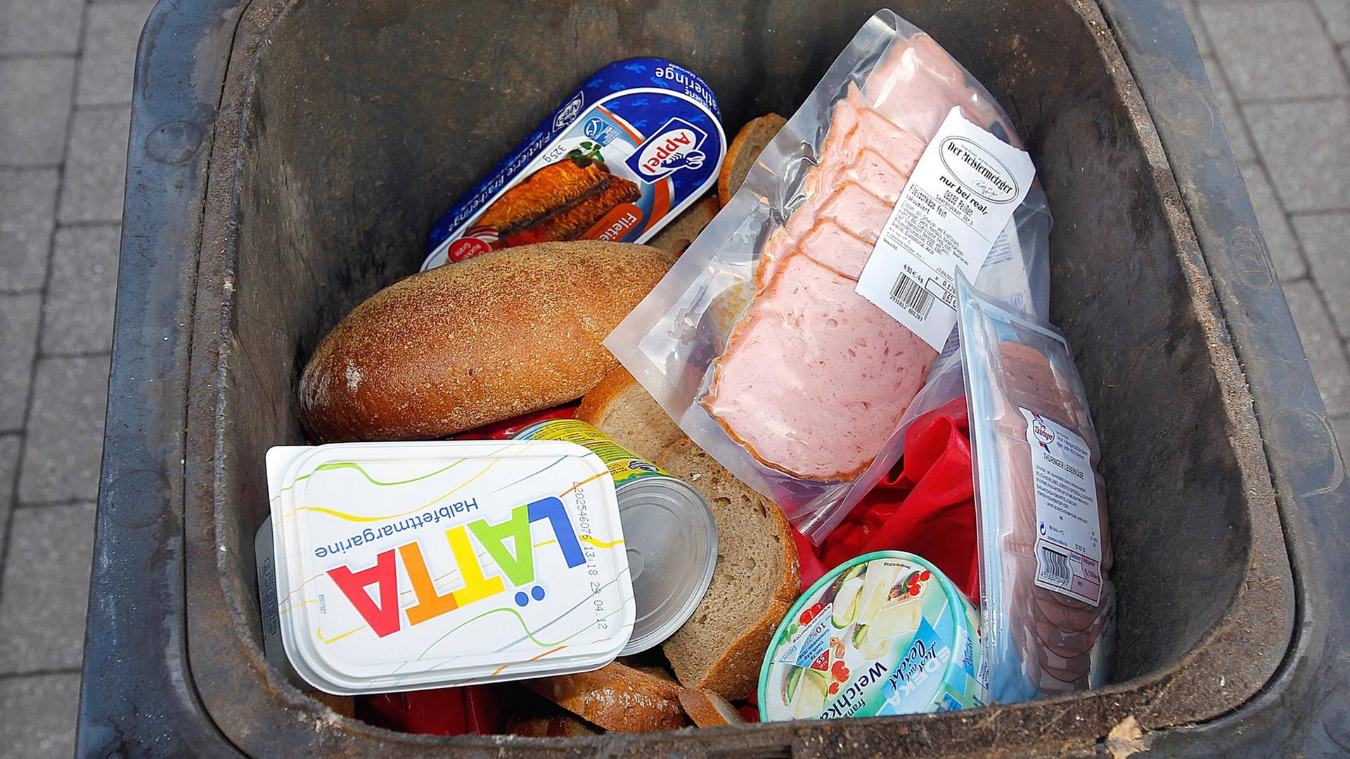 Eine Mülltonne ist bis zum Rand mit teilweise noch verpackten Lebensmitteln gefüllt.