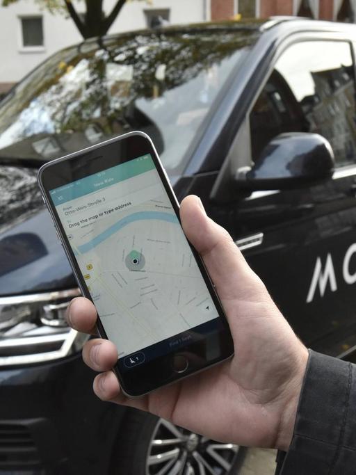 Ein Handy mit der MOIA-App vor einem Fahrzeug des Unternehmens.