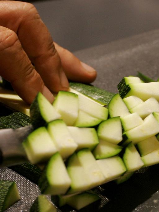 Zucchini wird auf einem Brettchen in kleine Würfel geschnitten,