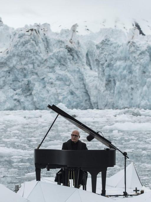 Ludovico Einaudi sitzt an einem Flügel, der auf einer Plattform im eisschollendurchsetzten Meer schwimmt, im Hintergrund Eisberge