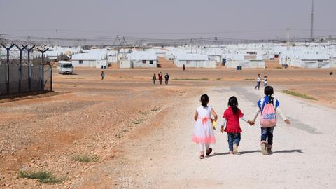 Drei Kinder laufen auf einer staubigen Straßen des Flüchtlingscamps Azraq in Jordanien und halten dabei die Hände.