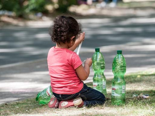 Ein Flüchtlingskind sitzt in Berlin auf dem Gelände des Landesamtes für Gesundheit und Soziales auf einem Grünstreifen.