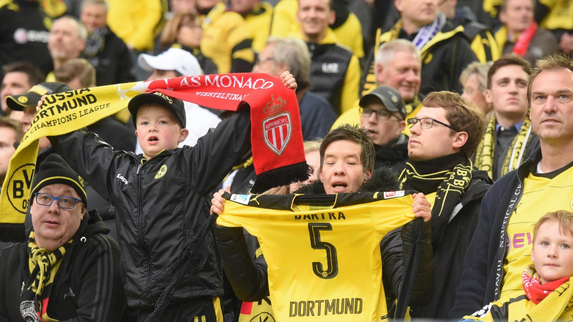 Dortmund-Fans auf der Tribüne. Ein Junge hält einen Fan-Schal mit Borussen- und Monaco-Logo. Dortmund-Fans auf der Tribüne. Ein Junge hält einen Fan-Schal mit Borussen- und Monaco-Logo.