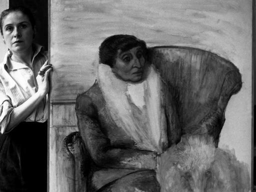 Dora Maar in ihrem Atelier, neben einem Gemälde, das eine ältere Frau in einem Sessel zeigt.