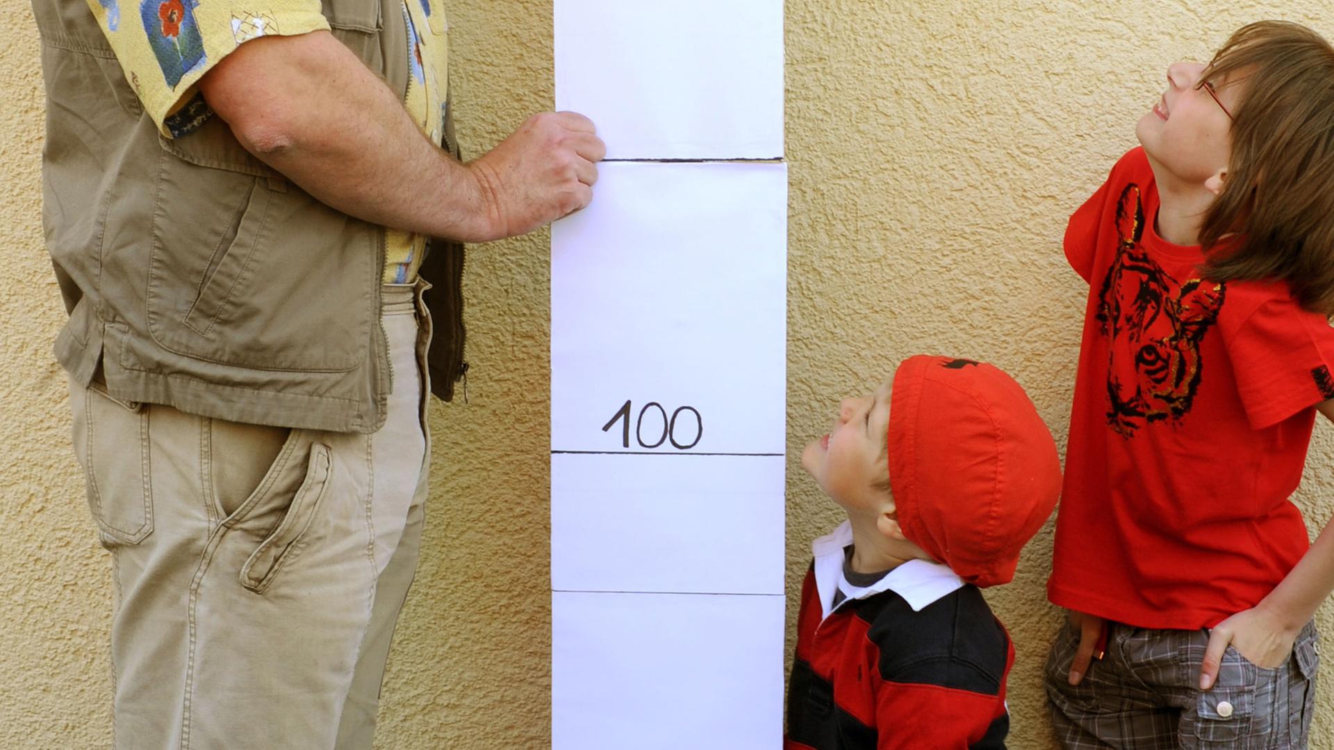 Zwei Kinder (4 und 7 Jahre alt) bewundern an einer Messlatte ihren großen Vater (2,06 Meter)