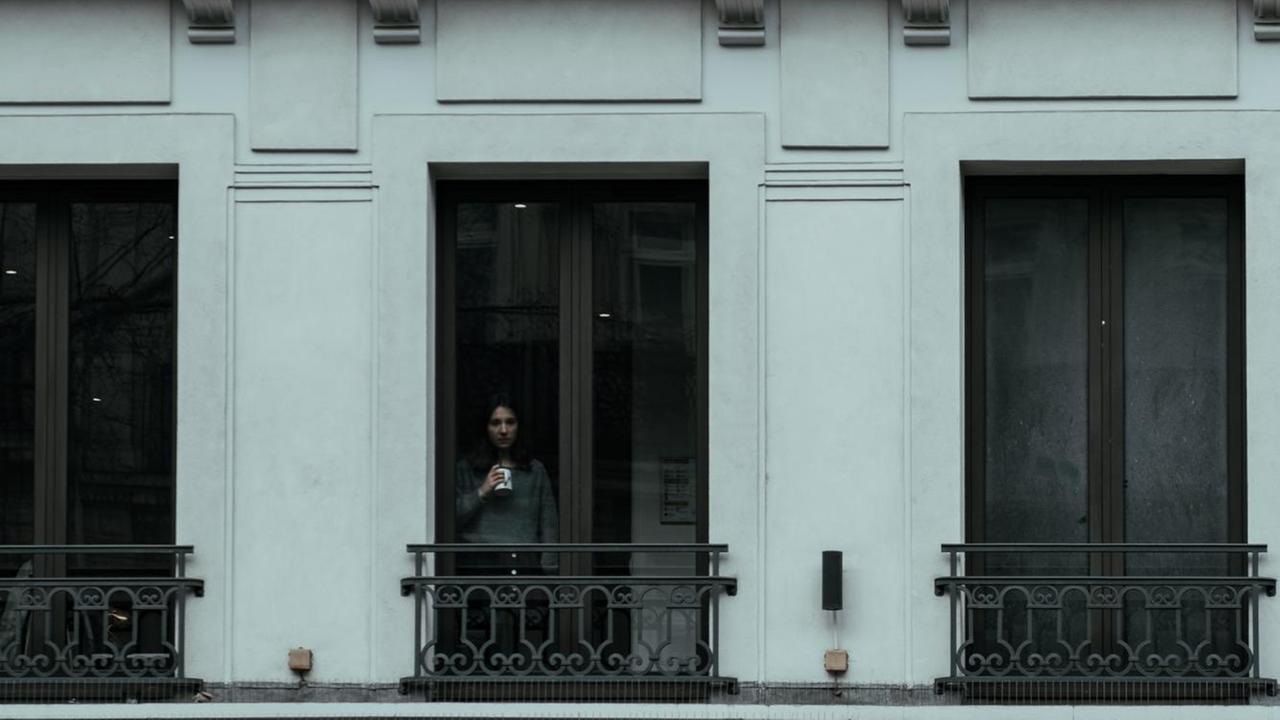 Eine Frau steht mit einer Tasse in der Hand an einem Fenster. Eine Frau steht mit einer Tasse in der Hand an einem Fenster.