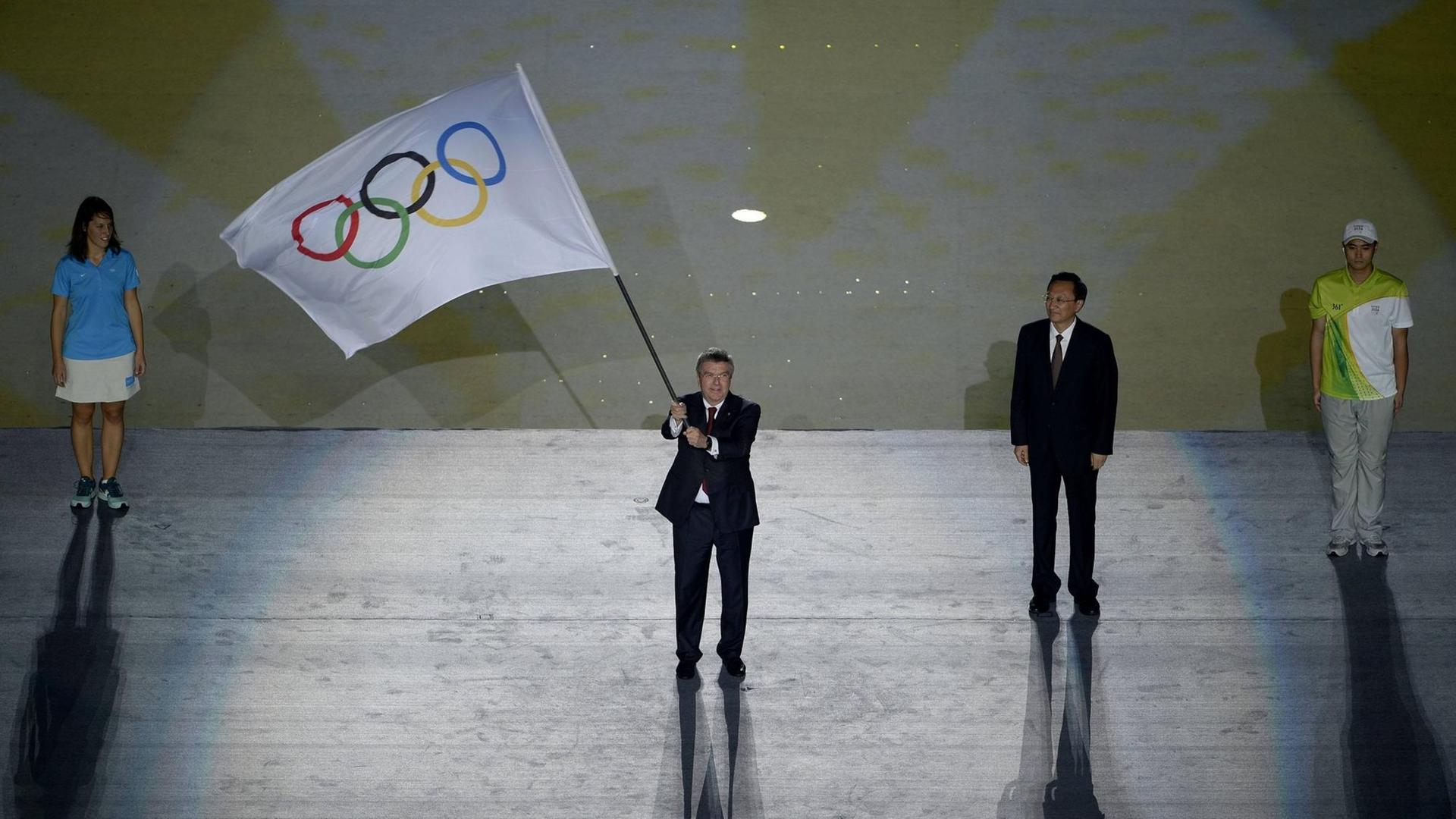 IOC-Präsident Thomas Bach schwenkt bei der Abschlusszeremonie der Olympischen Jugendspiele 2014 in Nanjing die Olmypische Flagge.