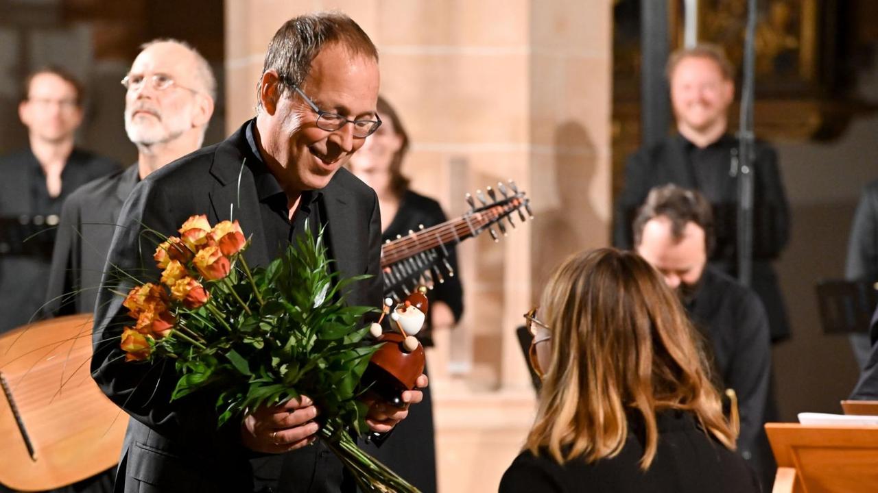 Ein Dirigent erhält einen Straus mit gelben Rosen und einen Räuchemann, der Paukenschlegel in der Hand hält. Ein Dirigent erhält einen Straus mit gelben Rosen und einen Räuchemann, der Paukenschlegel in der Hand hält.