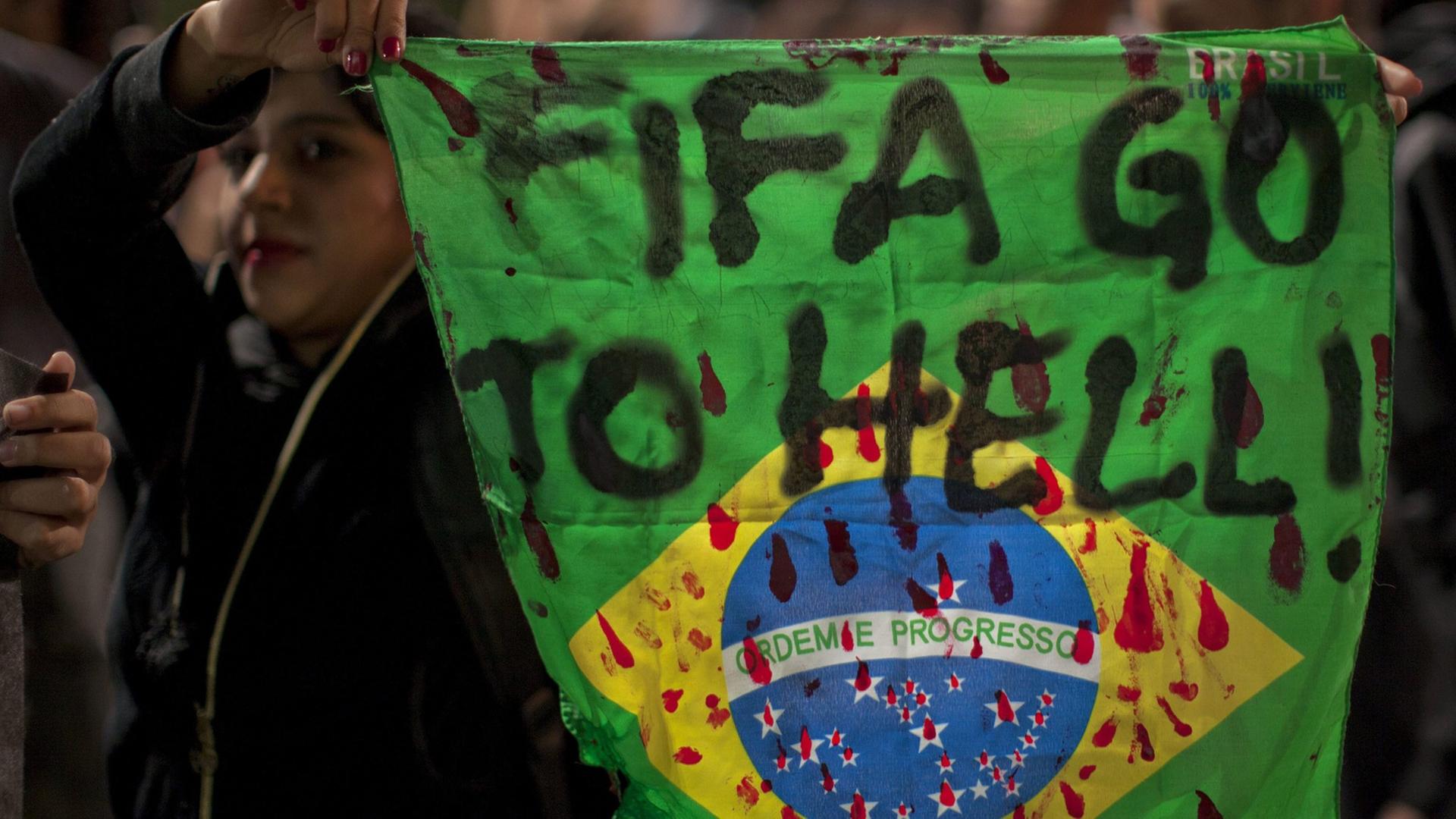 Eine Demonstrantin hält in Sao Paula eine Fahne Brasiliens mit der Aufschrift "Fifa, fahre zur Hölle!" in die Höhe. Eine Demonstrantin hält in Sao Paula eine Fahne Brasiliens mit der Aufschrift "Fifa, fahre zur Hölle!" in die Höhe.