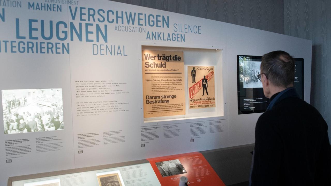 Ein Mann steht vor einer Informationswand, die zahlreiche historische Dokumente zeigt. Ein Mann steht vor einer Informationswand, die zahlreiche historische Dokumente zeigt.