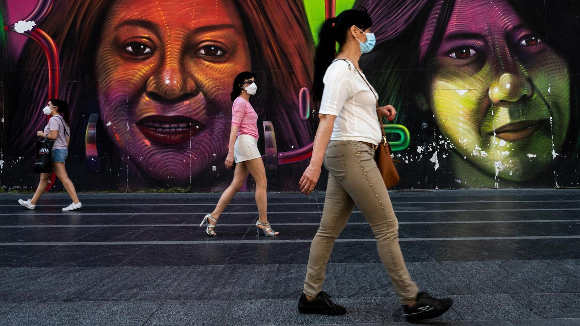 Drei Frauen gehen mit großem Abstand zueinander an einem bunten Graffito in Madrid vorbei. Drei Frauen gehen mit großem Abstand zueinander an einem bunten Graffito in Madrid vorbei.