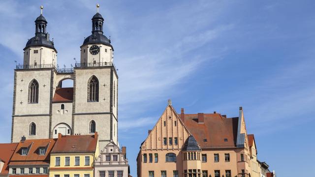 Zeile mit alten Häusern und der Stadtkriche in Wittenberg vor blauem Himmel