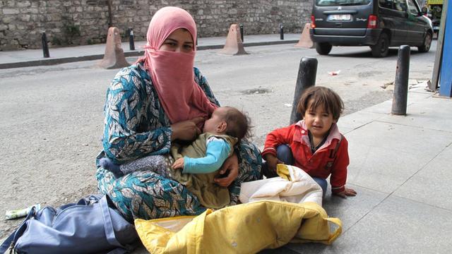 Eine syrische Frau sitzt mit zwei Kindern an einer Straße in Istanbul und bettelt.